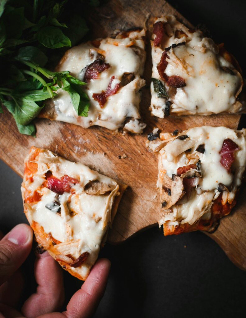 Delicious pizza slices with mozzarella, bacon, and herbs on a wooden board.